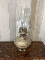 Full view of vintage Aladdin oil lamp showing the metal body and clear glass chimney on a wooden surface.