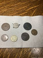 Overview of all 7 coins on white cloth, showing variety in size, design, and wear.