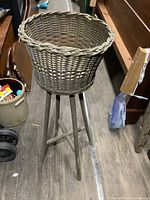 Overall view of the antique wooden plant stand with the wicker basket on top, showing the tripod wooden base on a wooden floor.