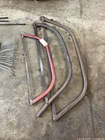 Three bow saws of different sizes on a ground surface, showing metal frames and saw blades with visible rust and wear.