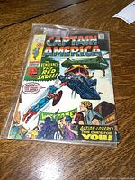 Image showing front cover of Captain America comic book stored in a plastic sleeve on a wooden surface.