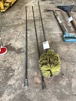 Photo showing the chimney sweep brush and three long metal rods with threaded connectors on ends, laid out on a concrete floor with a rake and other tools nearby.