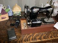 Front view of the black Cinderella sewing machine with floral patterns, motor attached and foot pedal beside it on a wooden table.