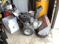 Front angle view showing the snowblower housing, tires, and engine with fuel tank and control cables.