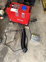 Red Vevor diesel space heater unit with blue fuel cap and control box connected, shown from front angle on concrete floor.