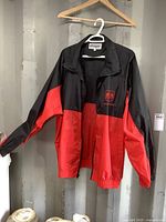 Full view of men's black and red Dodge windbreaker jacket hanging on a hanger showing front and sleeves.