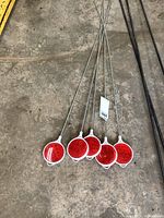 Photo showing all five driveway markers laid out on concrete floor, displaying red reflectors and long metal stakes.