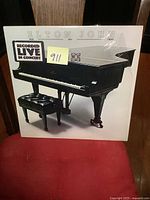 Front cover of the Elton John 'Here and There' LP album featuring a grand piano and a sticker 'Recorded Live in Concert'.