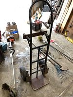 Front view of the black metal convertible hand cart with two large tires and a metal platform base, showing rust and wear.