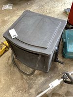 Gray resin hose reel box with basket-weave design, crank handle on the side and hose extending from the front, lid not attached