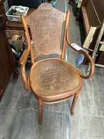 Front view of carved wooden armchair with curved armrests and detailed floral and face motifs on seat and backrest.