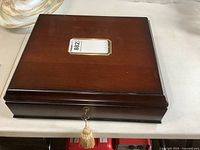 Top view of closed wood jewelry case with lock, key, tassel, and monogrammed surface.