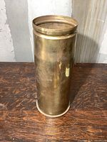 Front side view of the tall heavy brass military shell casing standing vertically on a wooden surface.