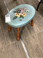 Front angled view of the vintage wooden milking stool with blue painted seat and floral design