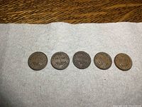 Five Newfoundland one cent coins dated 1938, 1940, 1941, 1942, and 1944 arranged in a row on a wooden surface with a white cloth beneath them