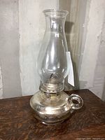 Full view of the vintage oil lamp showing clear glass chimney and metal base with handle.