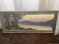 Full view of old oil painting on board showing landscape with trees, water, and mountains in an ornate frame.