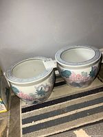 Photo of both porcelain planters side by side on a striped rug, showing round shape and floral decorations