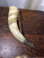 Full view of the powder horn showing natural cow horn material with attached leather strap.