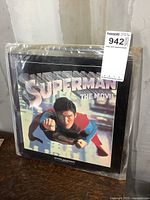 Front cover of Superman The Movie LaserDisc set showing Superman flying with arm extended, enclosed in clear plastic sleeve keeping the set protected.