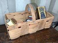 View of vintage woven wooden basket showing large handle and contents including jars and tins
