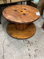Full side view of round wooden cable spool coffee table showing top surface, central core, and flat circular base. Visible wear and wood grain present.