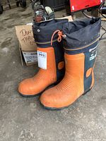 Pair of orange and black men's work boots with steel toes, showing signs of use, brand Husqvarna visible on boots.