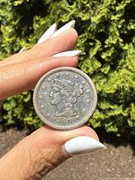 Obverse side of the 1849 USA one cent coin held between fingers showing Lady Liberty with 13 stars and date 1849.