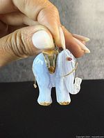 Pendant held between fingers against dark background showing front face with agate stone and gold details, ruby eye visible.