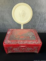 Red celluloid dresser box with silver inlay showing floral and scenic patterns on lid and sides.