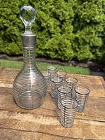 Full set of antique Art Deco decanter with six matching glasses on wooden surface outdoors.