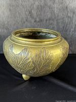 Front angle of antique bronze vessel showing rounded form and raised leaf motifs.