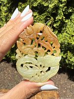 Front view of the two-tone carved jade pendant showing detailed leaves and floral design with gold bail attached.