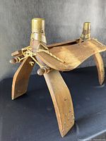 Front and side view of antique wooden saddle display stand with brass accents, showing curved seat and splayed legs with nail detailing.