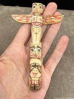 Hand-held close-up of small carved and painted wooden totem pole showing bird with wings outspread and painted detail.