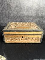 Front view of the carved sandalwood box showing detailed floral carvings and keyhole.