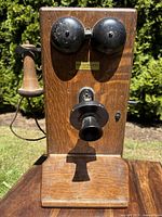 Front view of entire wooden wall-mounted telephone with black bells, mouthpiece, and side earpiece.