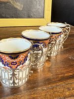 Four Aynsley Imari demitasse cups shown in a line, highlighting the blue and red Imari pattern with silver trim and holder detail.