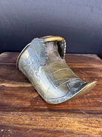 Angled view of bronze stirrup showing shell motif and embossed details.