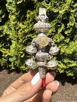 Front view of coral-handled rattle showing ornate silver top, mounted coin, dangling bells and red coral handle.