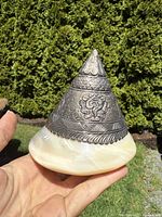 Side profile of the ritual object showing the conical sterling silver top with floral and Buddhist symbol carvings attached to a polished shell base.