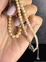 Close-up view of string of graduated natural pearls and sterling silver clasp detail in hand.