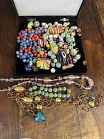 Top down view showing numerous colorful loose antique beads including round, cylindrical, and irregular shapes inside a black box with a few loose strands laying out.