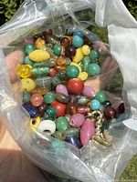 Plastic bag held in hand with a variety of antique Peking-glass beads visible, showing multiple colors and shapes.
