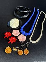 Photo showing entire collection of 13 antique plastic/celluloid jewelry pieces arranged on a black surface, including earrings, bracelets, brooches, and necklaces in various colors and styles.