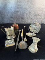 Overview of 9 antique sterling silver table items including matches box, ladle, knife, salt cellar, spoon, clip, and other ornamental objects.