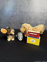 Front view of all four toys including two mohair dogs, plush mouse, and vintage bus model on yellow base