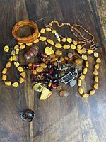 Top-down photo showing assorted amber jewelry pieces spread out on table including necklaces, bracelets, pendants, and loose beads.