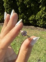 Close-up of the amethyst ring held between thumb and forefinger outside in natural light showing stone and band color.