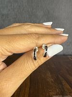 Pair of sterling silver half-hoop stud earrings held between fingers showing size and detail of black stones along the front.